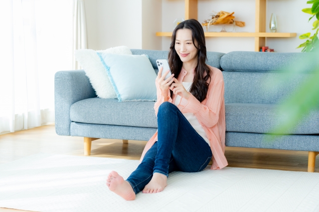 リビングで笑顔でスマホを見ている女性